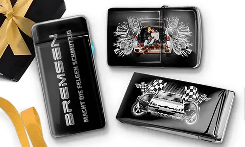 Elegante schwarze Feuerzeuge mit Auto-Designs. Eines zeigt eine Familie in einem Auto, ein anderes ein blaues Auto mit karierten Flaggen. Daneben liegt eine Geschenkbox mit goldener Schleife.