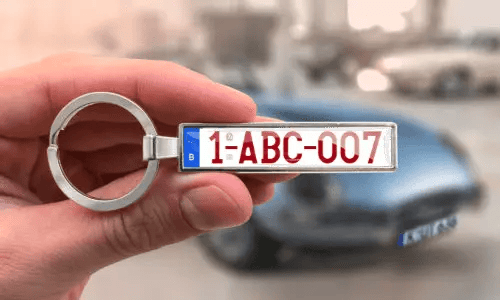 Sleutelhanger met aangepaste kentekenplaat, vastgehouden in de hand met auto op de achtergrond