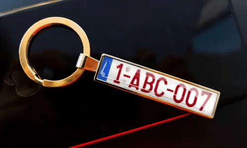 License plate keychain attached to keys in pocket with car in background