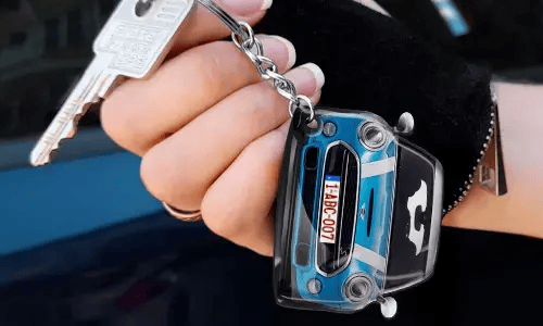Käsi pitää avaimenperää, joka on muotoiltu siniseksi autoksi yksityiskohtaisella etuosalla