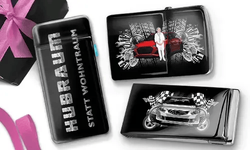 Drei Zigarettenetuis in Schwarz und Silber mit dynamischen Auto-Grafiken. Eines trägt die Aufschrift „Hubraum statt Wohntraum“, während die anderen Rennmotive zeigen.