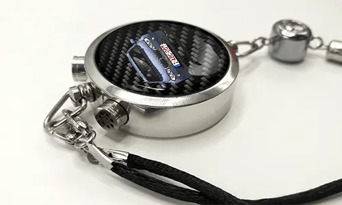 Round car key fob with carbon fiber face, buttons labeled LOCK and UNLOCK, braided black cord attached