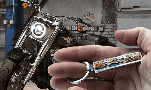 Portachiavi in metallo in stile fumetto con illustrazione di motocicletta, tenuto in mano vicino alla moto